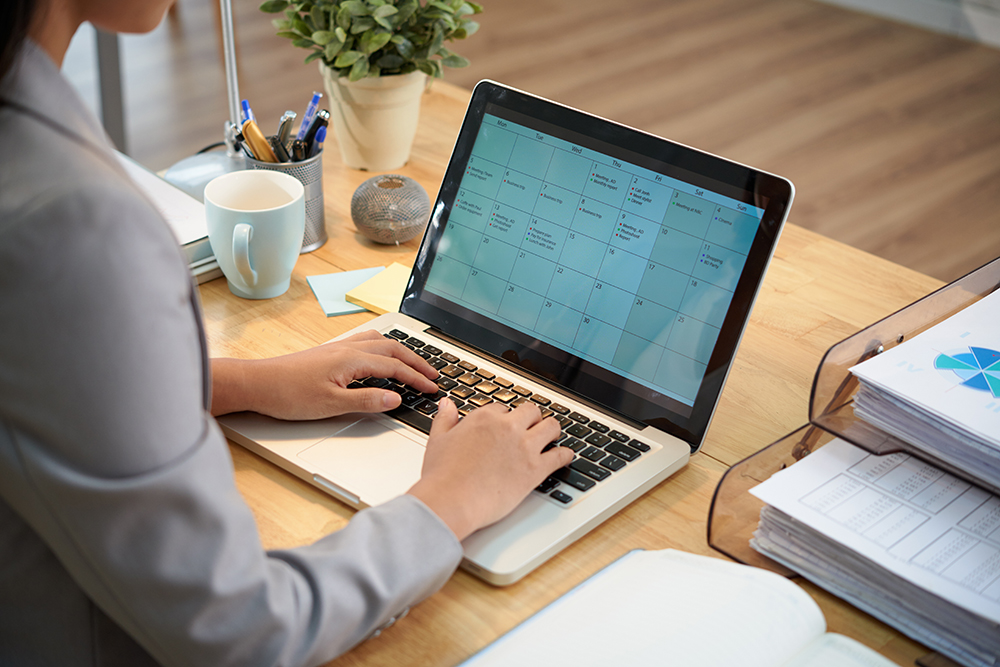 unrecognizable-businesswoman-sitting-desk-with-laptop-looking-calendar